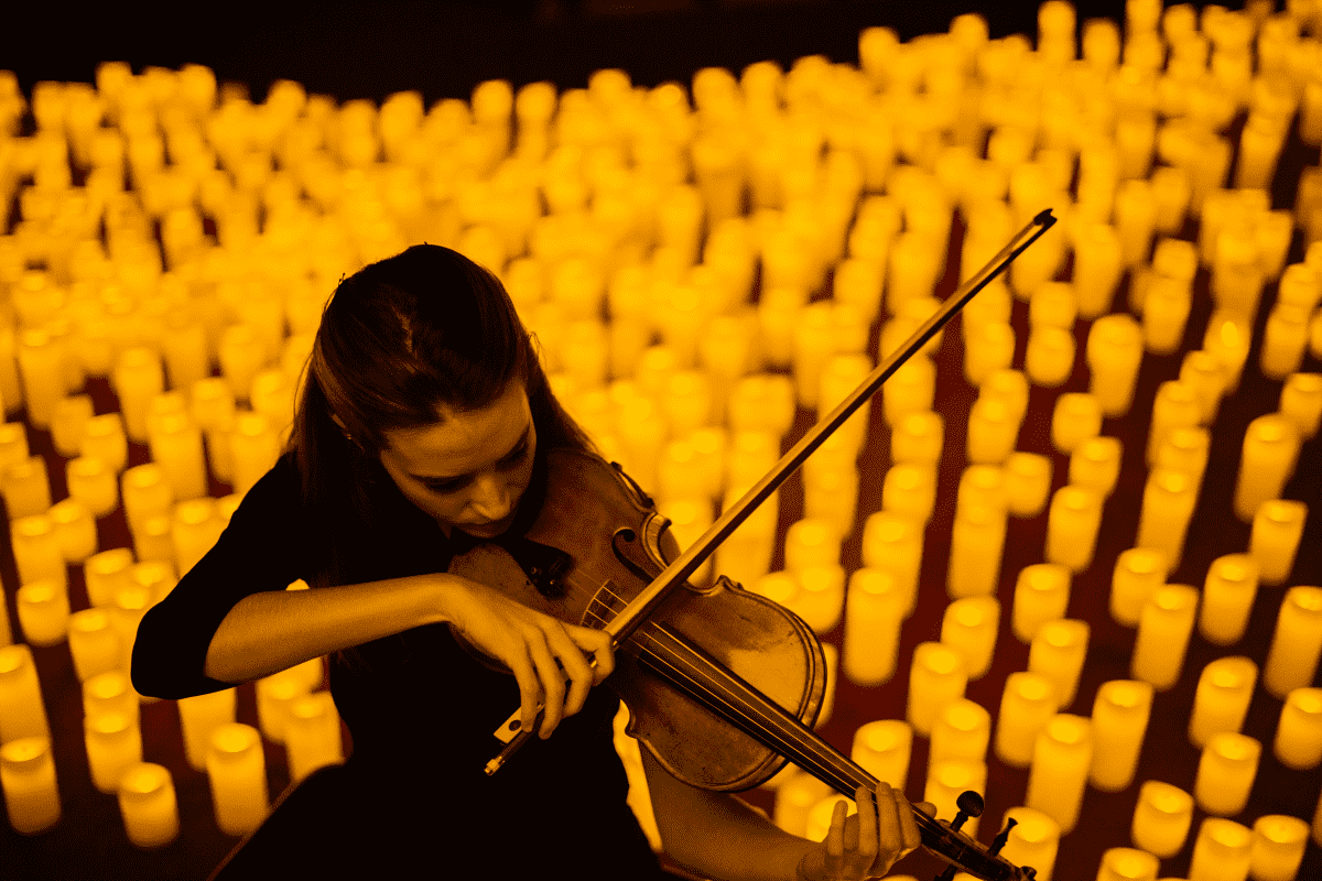A woman playing the violin with hundreds of candles in the background.