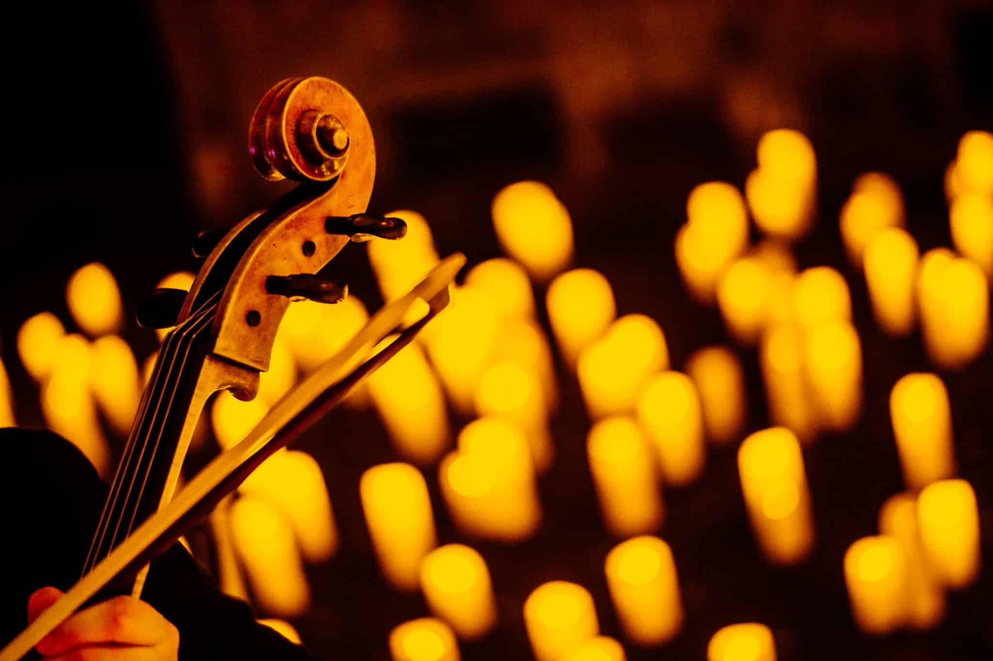 The top of a violin and a bow with the blurry image of candles in the background.